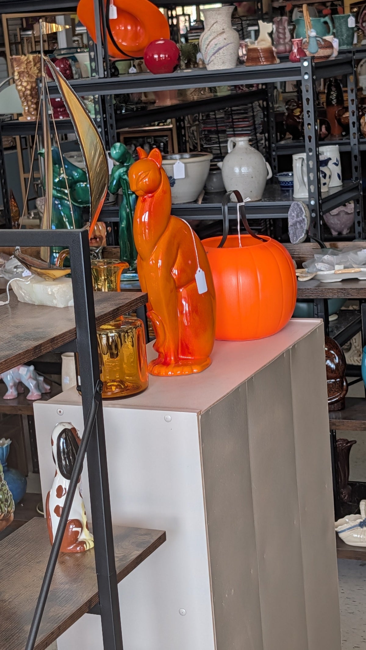 Orange Royal Haeger winking cat on a white pedestal in a Vintage Vibes booth, seen through the store window