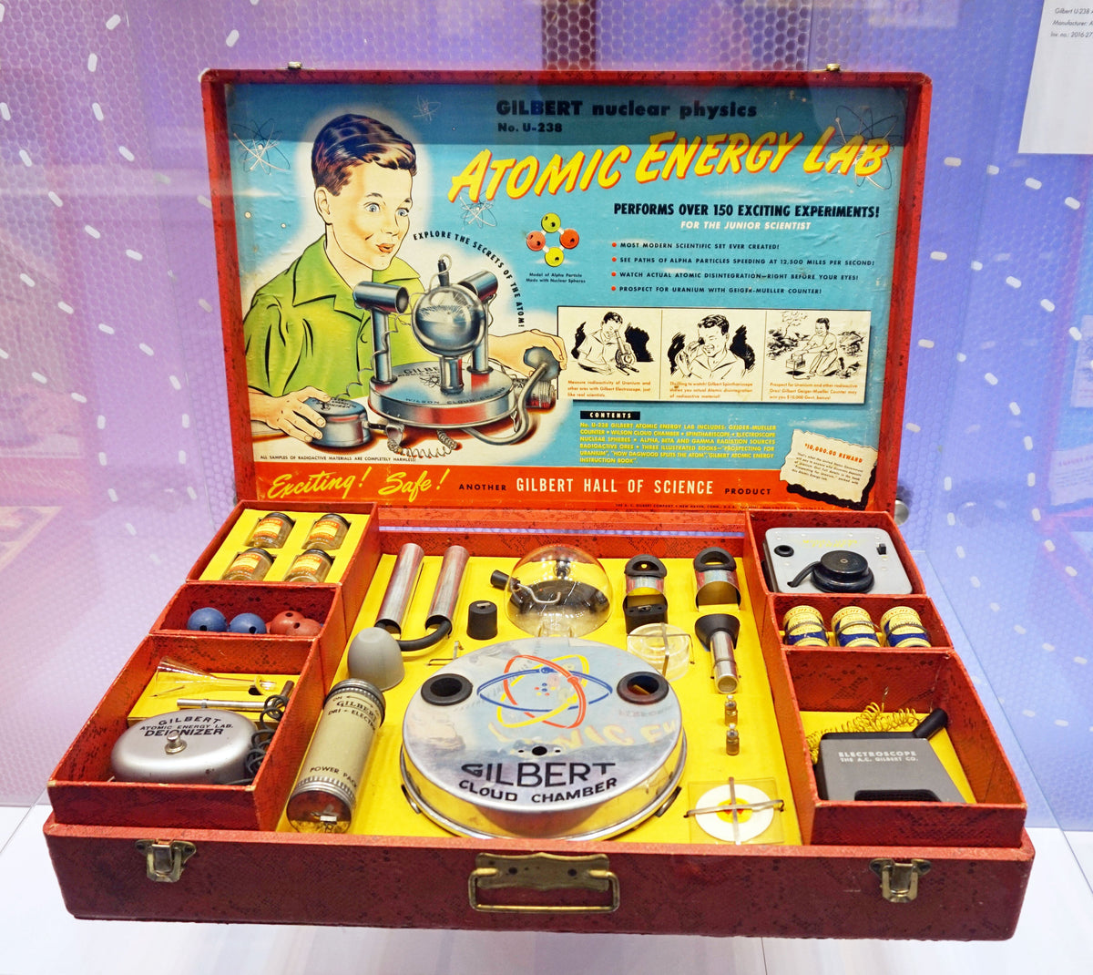 A Gilbert U-238 Atomic Energy Lab open in its case, showing the instruments, ore jars and manual